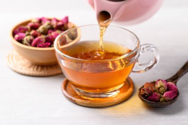 Çaydanlıktaki gül tomurcuğu çayı bardağa dökülüyor beyaz arka planda, sağlıklı çiçek çayı