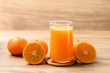 Bir bardak portakal suyu ve ahşap arka planda taze portakal suyu, sağlıklı bir içecek.