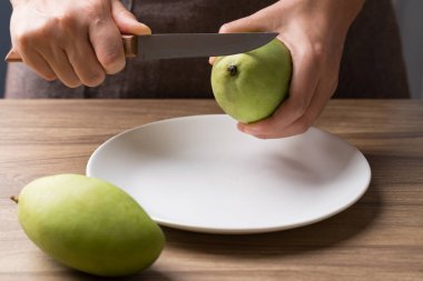 Mutfak bıçağını tutan ve salata yapmak için yeşil mango kesen.