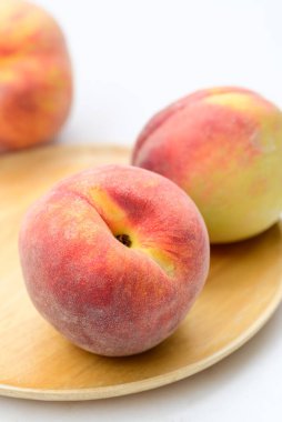 Şeftali meyvesi, tahta tabakta, beyaz arka planda.