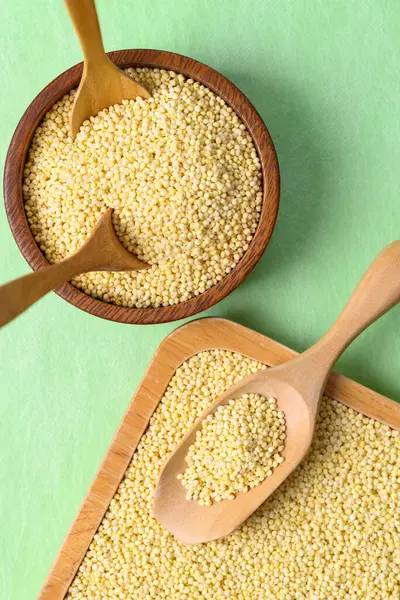 Tahta kasede sarı darı taneleri, yeşil arka planda kaşık, yiyecek malzemesi.