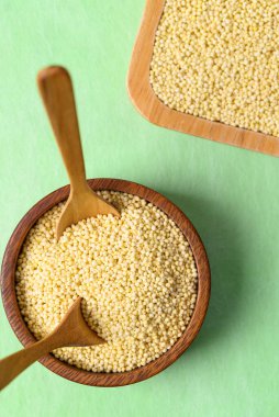Tahta kasede sarı darı taneleri, yeşil arka planda kaşık, yiyecek malzemesi.