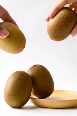 Tahta tabakla taze kivi meyvesi ve beyaz arka planda el, sağlıklı beslenme.