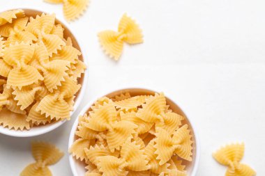 Beyaz arka planda basit beyaz bir kâse içinde çiğ farfalle makarna manzarası. Papyon biçimli makarna İtalyan mutfağının malzemelerini vurguluyor.