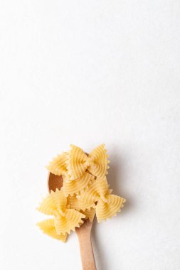 Beyaz bir arka plana yerleştirilmiş tahta kaşıkta çiğ farfalle makarna, İtalyan mutfak malzemelerini vurgulayan papyon şeklinde makarna ve minimal yemek tasarımı.