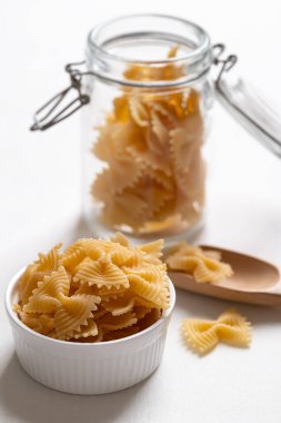 Beyaz bir kasede çiğ farfalle makarna ve beyaz arka planda cam kavanoz, papyon şeklinde makarna İtalyan mutfak malzemelerini vurguluyor.
