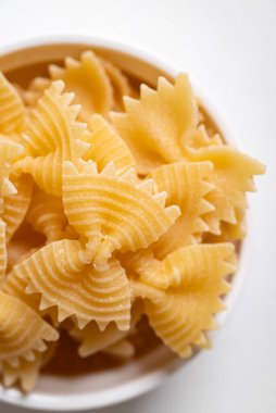Beyaz arka planda bir kasede çiğ farfalle makarna, papyonlu makarna İtalyan mutfak malzemelerini vurguluyor.