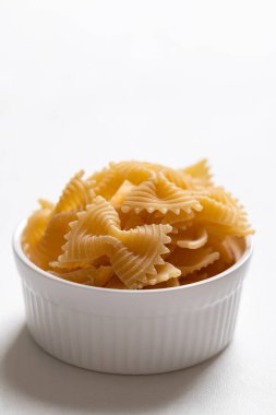 Beyaz arka planda beyaz bir kasede çiğ farfalle makarna, papyon şeklinde makarna İtalyan mutfak malzemelerini vurguluyor.