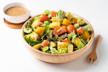 Beyaz arka planda Japon susamı soslu, saglikli, taze, bitkisel beslenme kavramına dayanan sade ahşap bir kasede renkli sebze salatası.