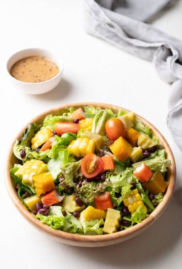 Beyaz arka planda Japon susamı soslu, saglikli, taze, bitkisel beslenme kavramına dayanan sade ahşap bir kasede renkli sebze salatası.