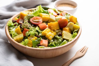 Beyaz arka planda Japon susamı soslu, saglikli, taze, bitkisel beslenme kavramına dayanan sade ahşap bir kasede renkli sebze salatası.