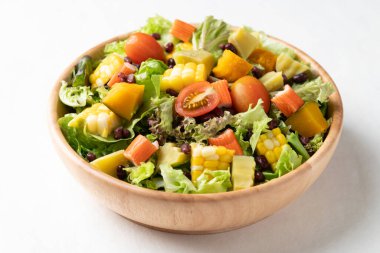 Beyaz arka planda kırsal ahşap bir kasede renkli sebze salatası sağlıklı, taze, bitki temelli yeme konsepti.