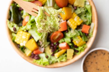 Beyaz arka planda Japonca susam soslu, ahşap bir kasede renkli sebze salatası sağlıklı, taze, bitki temelli yeme konsepti.