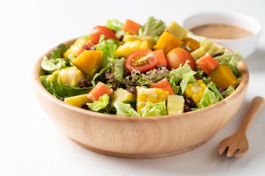 Beyaz arka planda Japon susamı soslu, saglikli, taze, bitkisel beslenme kavramına dayanan sade ahşap bir kasede renkli sebze salatası.