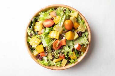 Beyaz arka planda kırsal ahşap bir kasede renkli sebze salatası, sağlıklı, taze, bitki temelli yeme konsepti.