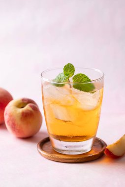 Buzlu şeftali çayı, bardakta nane yaprağı ve pembe arka planda taze şeftali, yaz içeceği.
