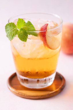 Buzlu şeftali çayı, taze şeftali dilimi ve pembe arka planda nane yaprağı, yaz içeceği.