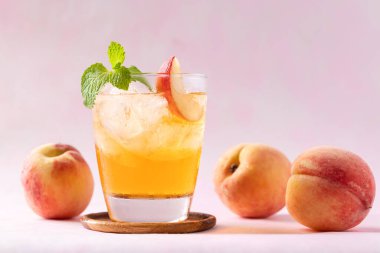 Buzlu şeftali çayı, taze şeftali dilimi ve pembe arka planda nane yaprağı, yaz içeceği.