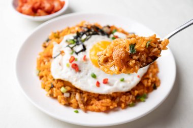 Kızarmış yumurta, domuz eti, susam tohumu, kırmızı biber, taze soğan ve beyaz tabakta deniz yosunu ile Kore kimchi pilavı.