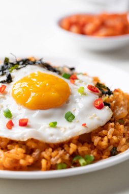 Kızarmış yumurta, domuz eti, susam tohumu, kırmızı biber, taze soğan ve beyaz tabakta deniz yosunu ile Kore kimchi pilavı.