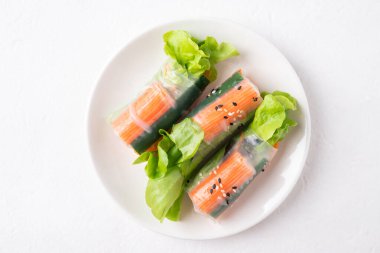 Yengeç sopası, havuç, salatalık, salatalık ve beyaz arkaplan üzerine pirinç kağıdı sarılmış marul.