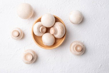 Beyaz arka plandaki ahşap kasede taze beyaz şampiyon mantarının (şişe mantarı) üst görüntüsü, yenilebilir mantar, yiyecek malzemeleri.