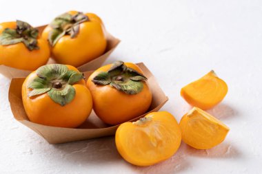 Beyaz arka planda, Kraft kağıt kasesinde taze olgun hurma, sonbahar tatlı meyvesi