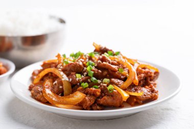 Beyaz arka planda pişmiş pirinç ve kimchi ile Kore usulü kızarmış baharatlı domuz eti (Bulgogi).