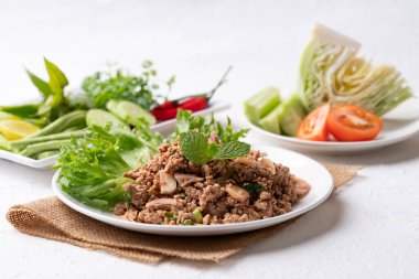 Yerel Tayland yemekleri, baharatlı domuz salatası (Larb Moo) beyaz arka planda taze sebzelerle yemek