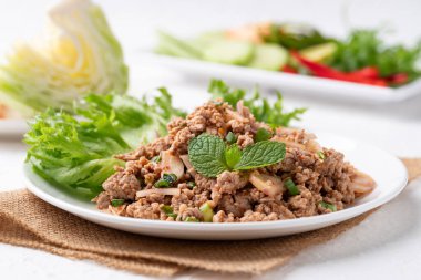 Yerel Tayland yemekleri, baharatlı domuz salatası (Larb Moo) beyaz arka planda taze sebzelerle yemek
