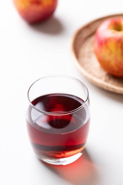 Beyaz arka planda kırmızı elma meyveli bir bardak elma şarabı.