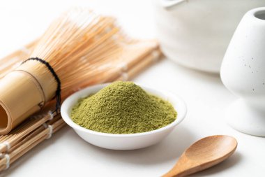 Tahta kaşıklı kibrit yeşil çay tozu, bambu çırpısı ve beyaz arka planda Chawan kasesi.