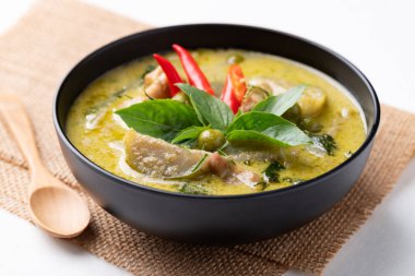 Siyah kasede yeşil körili tavuk ve beyaz arka planda kaşık.