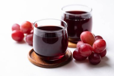 Bardakta kırmızı üzüm suyu ve beyaz arka planda taze üzüm meyvesi, sağlıklı içecek.