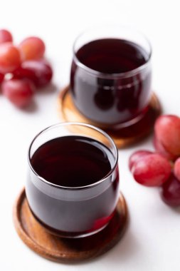 Bardakta kırmızı üzüm suyu ve beyaz arka planda taze üzüm meyvesi, sağlıklı içecek.