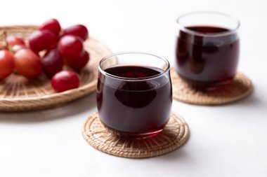 Bardakta kırmızı üzüm suyu ve beyaz arka planda taze üzüm meyvesi, sağlıklı içecek.