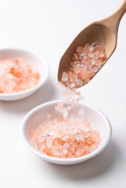 Himalaya pembe tuzu beyaz arka planda kaseye dökülüyor, sağlıklı besin maddeleri.