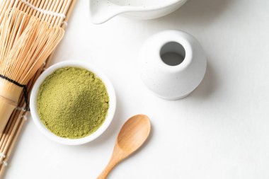 Tahta kaşıklı kibrit yeşil çay tozu, bambu çırpısı ve beyaz arka planda Chawan kasesi.