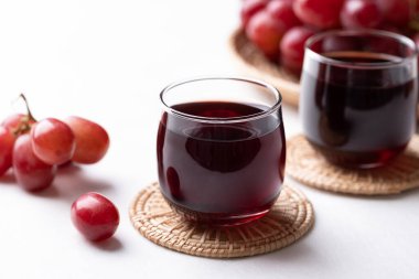 Bardakta kırmızı üzüm suyu ve beyaz arka planda taze üzüm meyvesi, sağlıklı içecek.