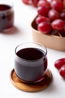 Bardakta kırmızı üzüm suyu ve beyaz arka planda taze üzüm meyvesi, sağlıklı içecek.