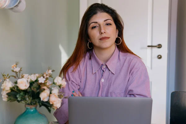 Young woman with serious look looks into camera - business woman at home with laptop