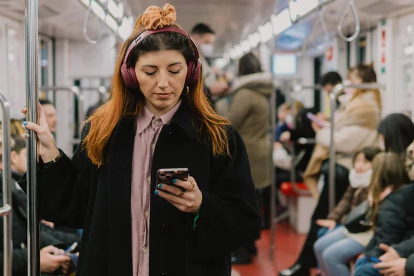 Portrait of young woman in subway listening to music in headphones and using smart phone