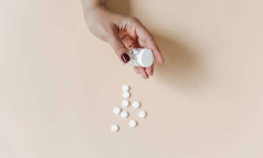 Bir şişe hap tutan bir kadın. Bej arka plan. Beyaz haplı ilaç şişesi. Üst görünüm