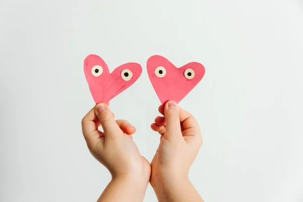 Hand made for Valentines or Mothers day. Two hand painted pink paper hearts with eyes in the child\'s hands. White background.