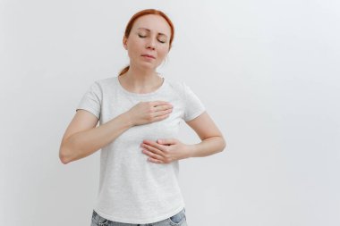 Young caucasian woman feeling breast pain, touching her chest. Brest cancer. White background, studio shoot.