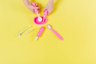 Kids hands with dentist set toy. Yellow background. Flat lay. Medical, stomatology, kids toys concept. Profession choice.