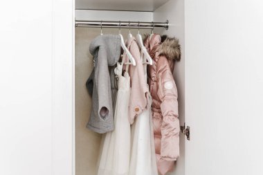 Hangers with stylish clothes for a girl in the white closet.