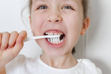 Küçük mutlu kızın portresi dişlerini pembe bir diş fırçasıyla fırçalar. Beyaz altyapı. Sağlık, diş sağlığı, kişisel hijyen konsepti. Yakın çekim görünümü