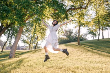Genç bir kadın yazın mutlu ve mutlu bir şekilde parka atlıyor. Yeşil ağaçlar, doğa ve güneş ışığı.