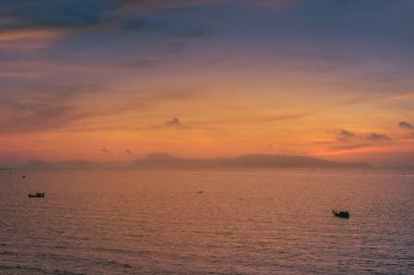 Beautiful cloudscape over the sea, sunrise shot. Lonely boats. Vung Tau beach, Vietnam with beautiful yellow sunrise sky, sun and clouds in orange and blue tones. Background and travel concept.
